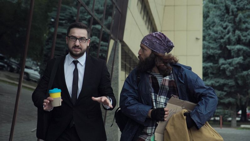 Dwóch mężczyzn idących obok siebie – jeden biznesmen z kawą w dłoni, drugi o wyglądzie człowieka bezdomnego - itogis.pl