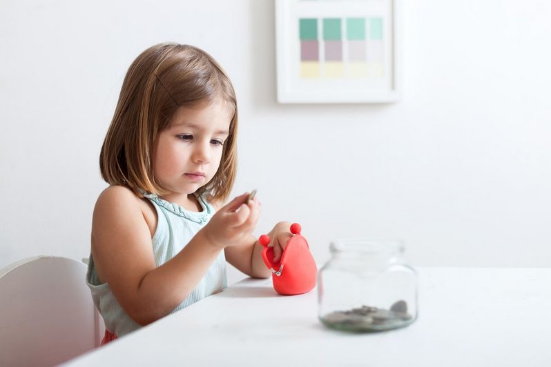 Kilkuletnia dziewczynka siedząca przy stole i bawiąca się monetami wyjmowanymi z czerwonego portfelika - itogis.pl