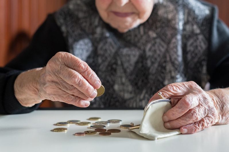 Starsza, biedna kobieta licząca monety wysypane z jej portmonetki na stół - itogis.pl